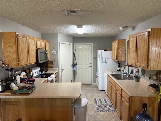 1227 Elmo Ln, San Angelo, TX 76905 - kitchen with white appliances, light countertops, a peninsula, a textured ceiling, and brown cabinets