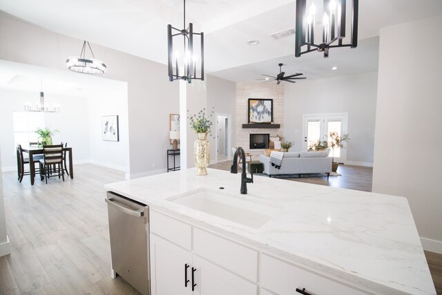 kitchen featuring visible vents, dishwasher, light wood-style floors, a fireplace, and a sink