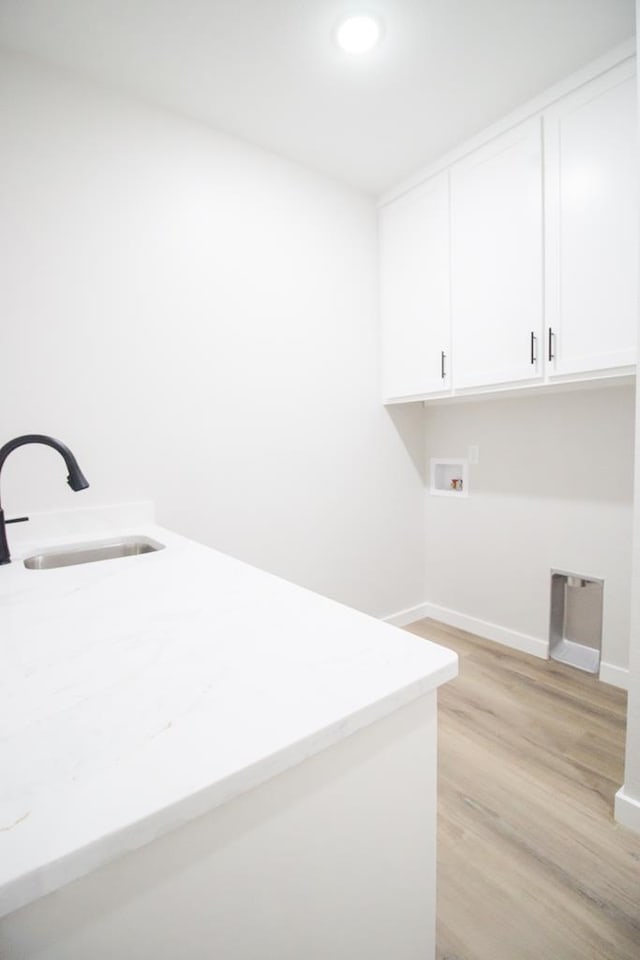 clothes washing area with washer hookup, cabinet space, light wood-style flooring, a sink, and baseboards