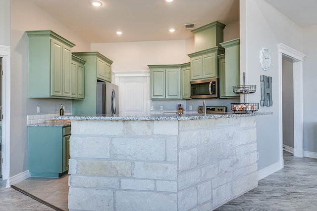 kitchen featuring visible vents, light wood-type flooring, stainless steel appliances, green cabinetry, and light stone countertops