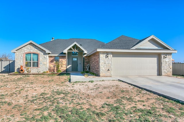 single story home with stone siding, fence, concrete driveway, an attached garage, and a shingled roof