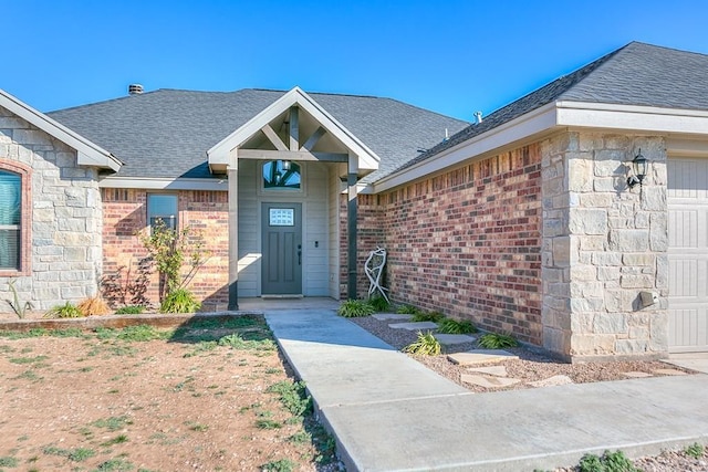 entrance to property with brick siding, an attached garage, and roof with shingles