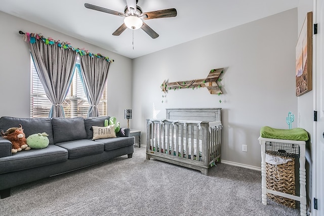 bedroom featuring a nursery area, baseboards, carpet, and ceiling fan