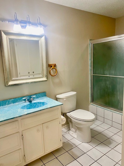 2608 Sunset Dr, San Angelo, TX 76904 - full bathroom with a shower with door, tile patterned flooring, toilet, vanity, and a textured ceiling
