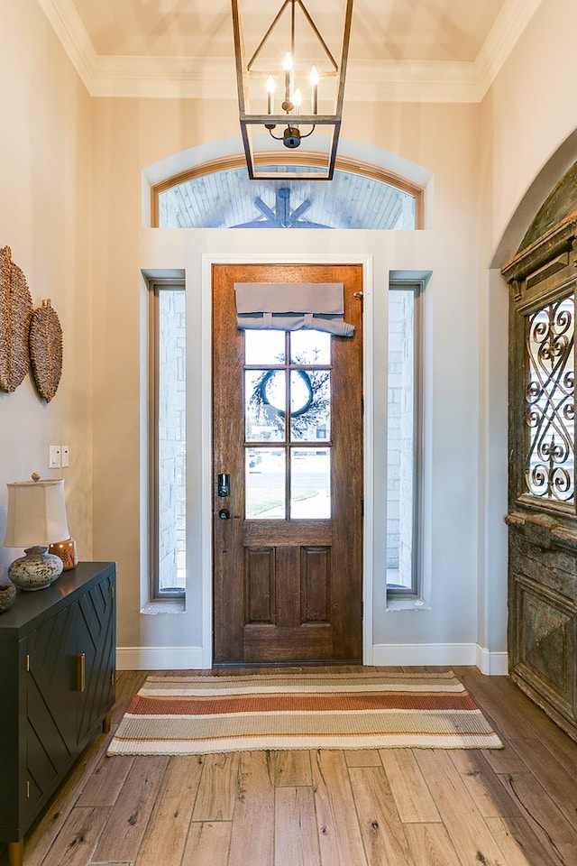 foyer with an inviting chandelier, crown molding, and wood-type flooring