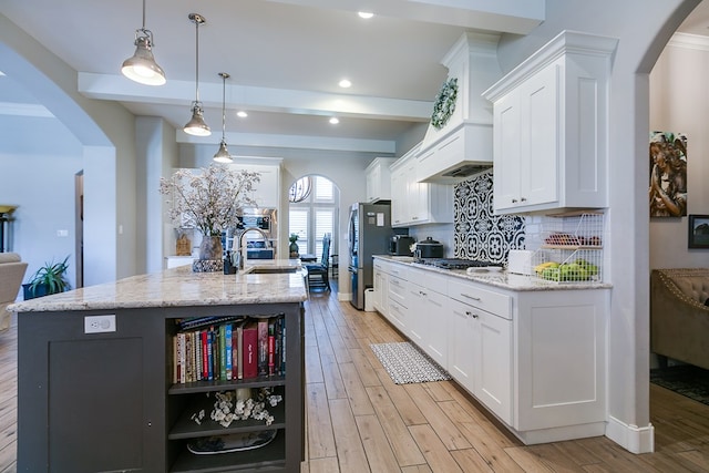 kitchen featuring stainless steel fridge, decorative light fixtures, a kitchen island with sink, and white cabinets