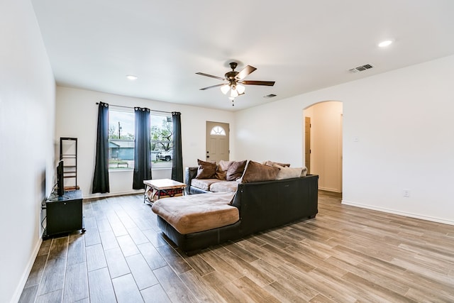 living area with visible vents, baseboards, wood finished floors, arched walkways, and a ceiling fan