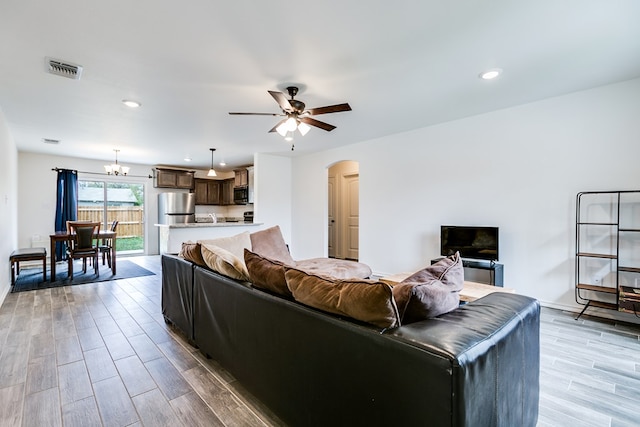 living area featuring arched walkways, visible vents, ceiling fan with notable chandelier, and light wood-type flooring