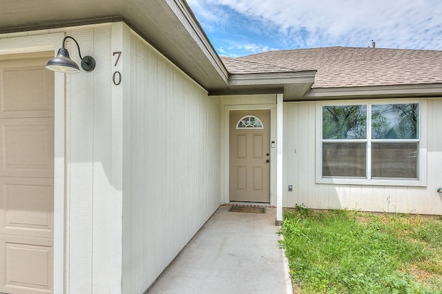 entrance to property with an attached garage and a shingled roof