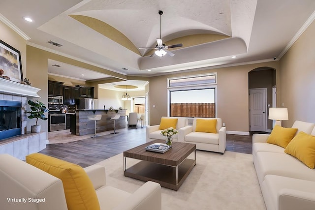 living area featuring a raised ceiling, arched walkways, visible vents, and a tile fireplace