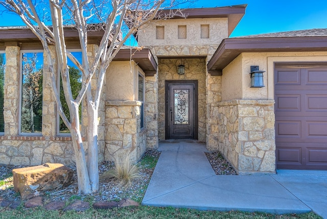 view of exterior entry with a garage, stone siding, and stucco siding