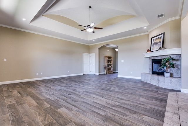 unfurnished living room featuring a tiled fireplace, visible vents, a raised ceiling, and a ceiling fan