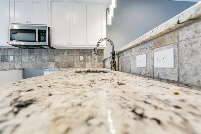 kitchen with sink, white cabinetry, backsplash, light stone counters, and decorative light fixtures