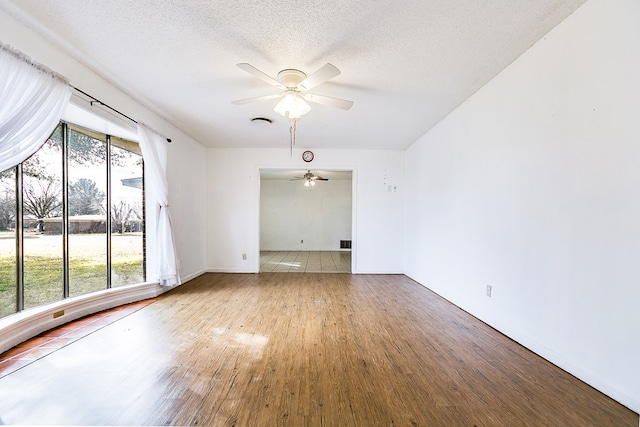 empty room with ceiling fan, plenty of natural light, hardwood / wood-style floors, and a textured ceiling