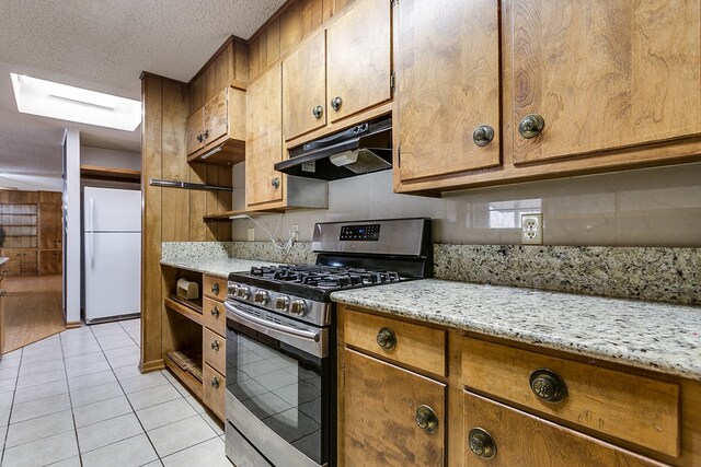 kitchen featuring light tile patterned floors, stainless steel range with gas stovetop, white refrigerator, light stone countertops, and a textured ceiling