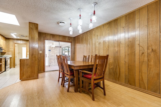 dining area with a textured ceiling, light hardwood / wood-style floors, and wood walls