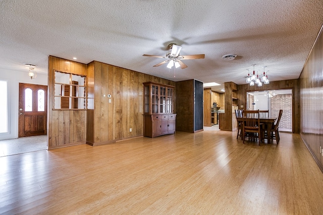 dining room featuring wooden walls, ceiling fan with notable chandelier, light hardwood / wood-style flooring, and a textured ceiling