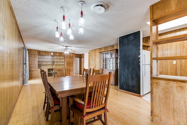 dining area with a textured ceiling, light hardwood / wood-style floors, ceiling fan, and wood walls