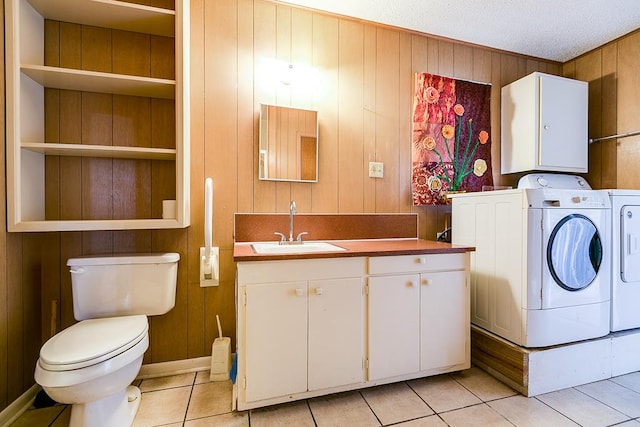 laundry room with light tile patterned flooring, washer and clothes dryer, sink, and wood walls