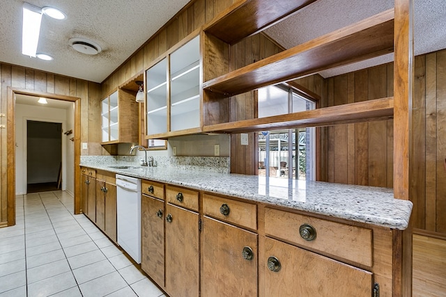 kitchen with dishwasher, sink, light stone countertops, and wood walls