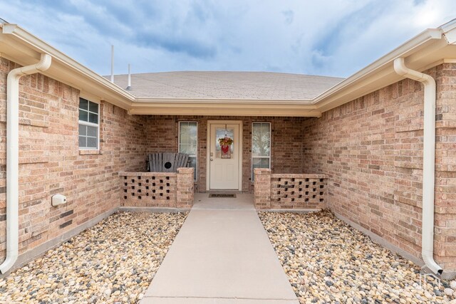 doorway to property with a shingled roof and brick siding
