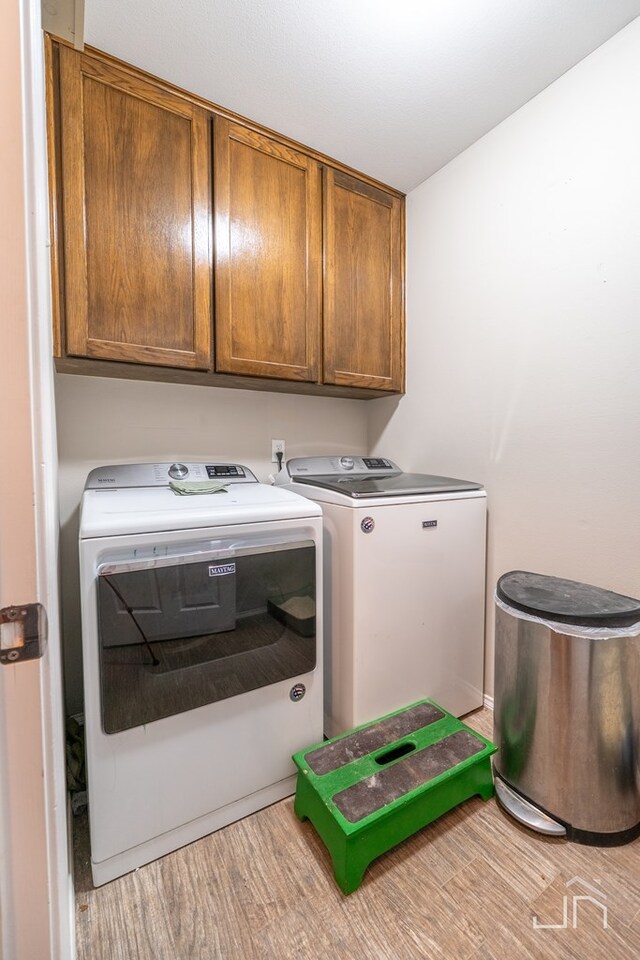 washroom featuring wood finished floors, washing machine and clothes dryer, and cabinet space