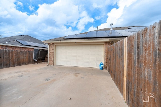 garage featuring solar panels, fence, and concrete driveway