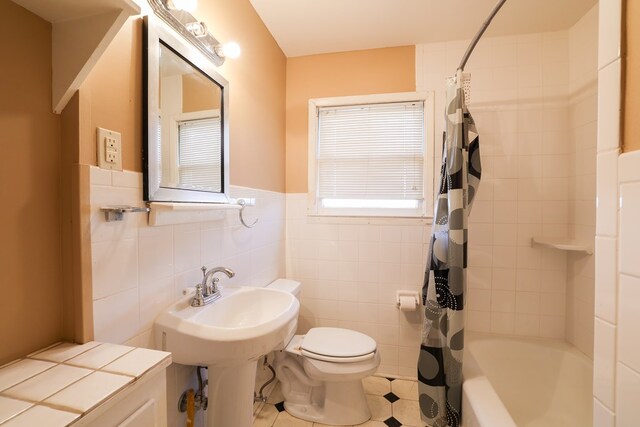 bathroom with tile walls, shower / bath combination with curtain, and toilet