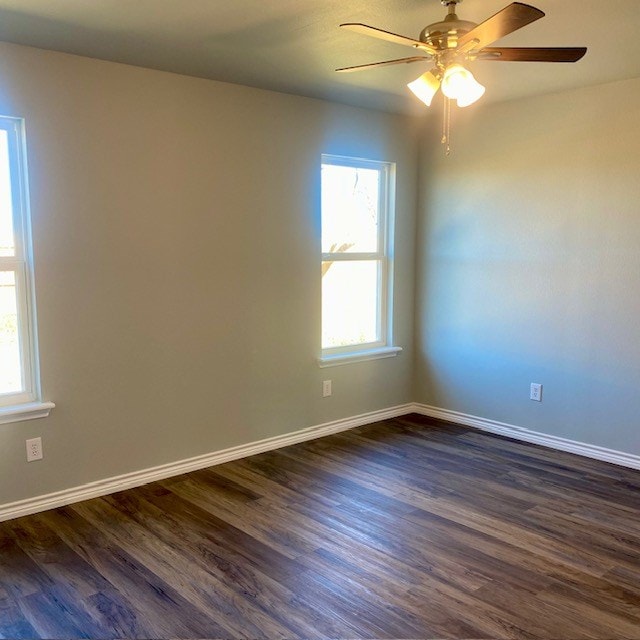 spare room with a ceiling fan, baseboards, dark wood-style flooring, and a wealth of natural light