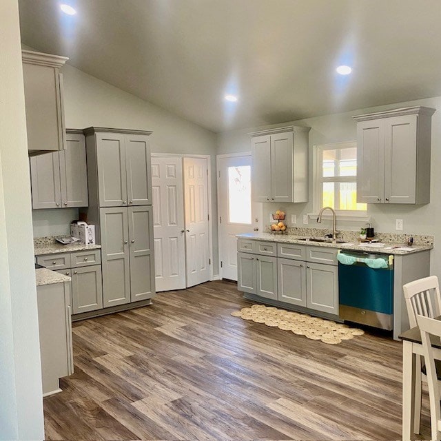 kitchen featuring dark wood-style floors, lofted ceiling, gray cabinetry, stainless steel dishwasher, and a sink