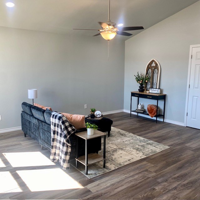 living room featuring lofted ceiling, ceiling fan, baseboards, and wood finished floors