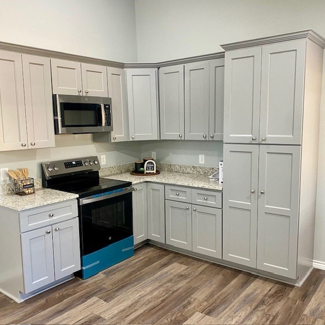 kitchen featuring stainless steel appliances, dark wood-type flooring, gray cabinets, and light stone countertops