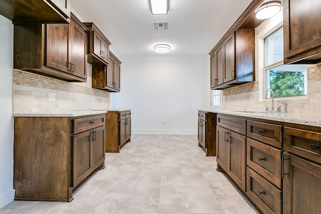 kitchen featuring light stone countertops, dark brown cabinetry, and decorative backsplash