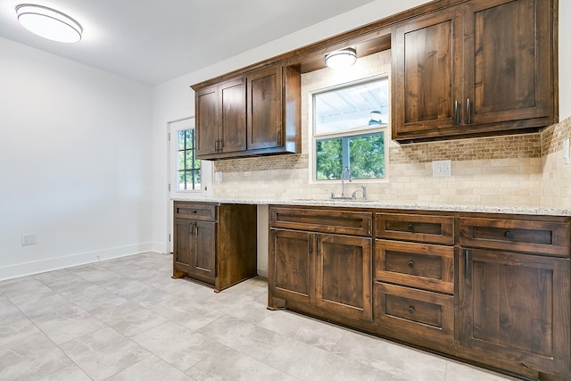 kitchen with light stone counters, sink, dark brown cabinets, and a healthy amount of sunlight