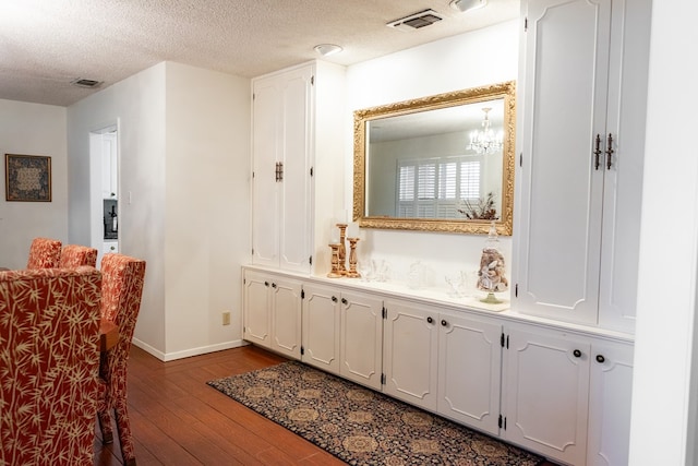 bathroom with a textured ceiling, vanity, wood finished floors, and visible vents