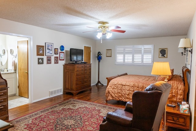 bedroom with ceiling fan, a textured ceiling, visible vents, and wood finished floors