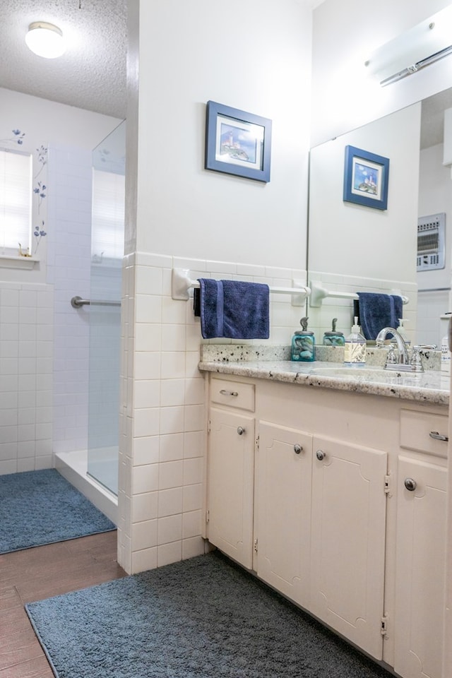 bathroom with a textured ceiling, vanity, tile walls, tiled shower, and wainscoting