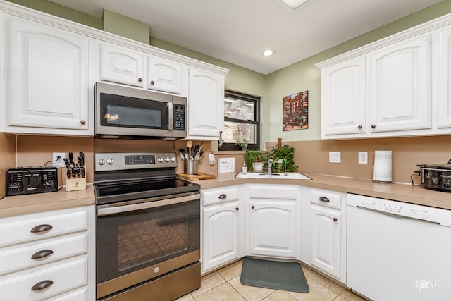 kitchen featuring stainless steel appliances, white cabinets, light tile patterned flooring, and a sink