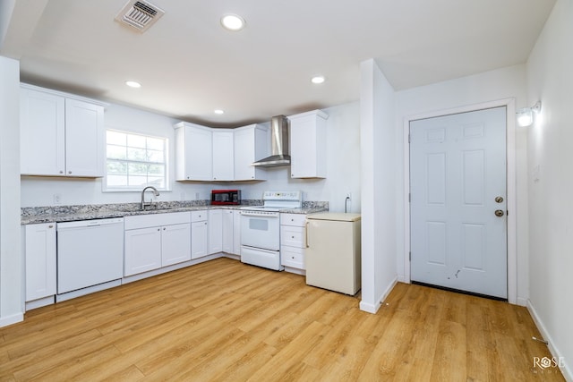 kitchen featuring white appliances, light stone countertops, light hardwood / wood-style floors, white cabinets, and wall chimney exhaust hood