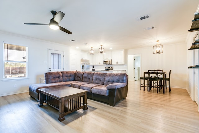 living room with crown molding, ceiling fan with notable chandelier, and light hardwood / wood-style flooring