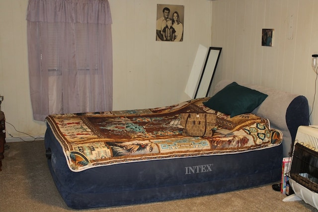 carpeted bedroom with heating unit and wood walls