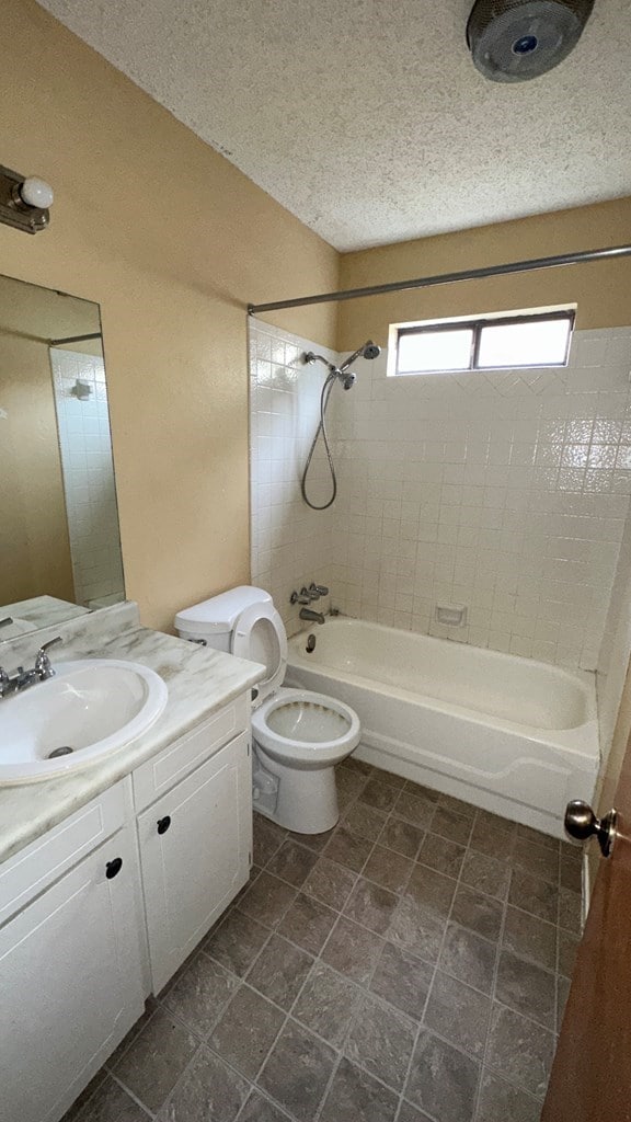 full bathroom with tiled shower / bath, vanity, toilet, and a textured ceiling