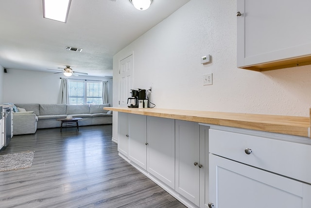 kitchen with ceiling fan, wood-type flooring, a textured ceiling, white cabinets, and wood counters