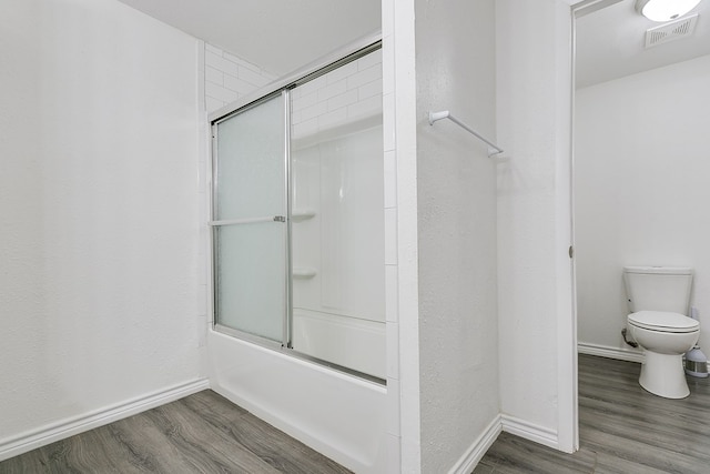 bathroom featuring hardwood / wood-style flooring, shower / bath combination with glass door, and toilet