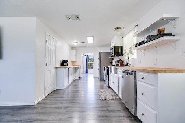 kitchen with wood-type flooring, appliances with stainless steel finishes, white cabinets, and butcher block countertops