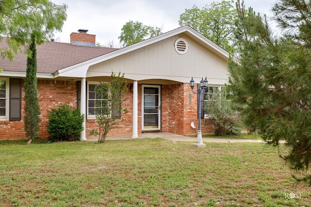exterior space featuring brick siding, roof with shingles, a chimney, and a lawn