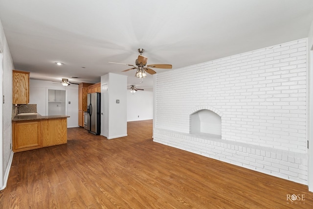 unfurnished living room with brick wall, baseboards, a ceiling fan, and dark wood-style floors