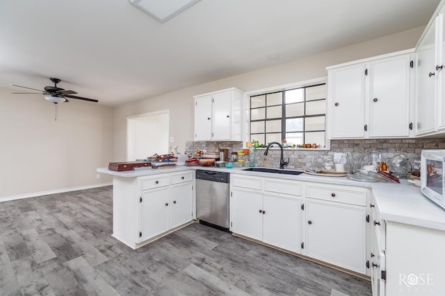 kitchen featuring a sink, light wood-style floors, dishwasher, a peninsula, and backsplash