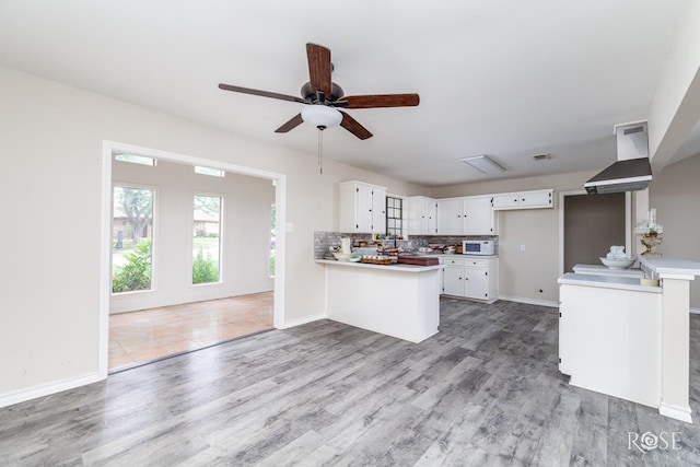 kitchen featuring a peninsula, light countertops, white cabinets, light wood finished floors, and backsplash