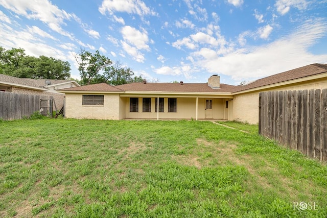 rear view of property featuring brick siding, fence, a yard, and a chimney